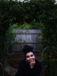 Portrait of smiling young woman sitting against trees in backyard