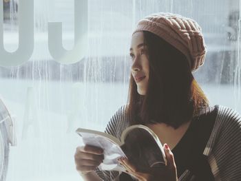 Close-up of young woman holding book while sitting by window