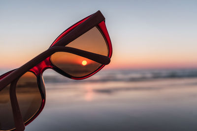 Close-up of sunglasses on beach against sky during sunset