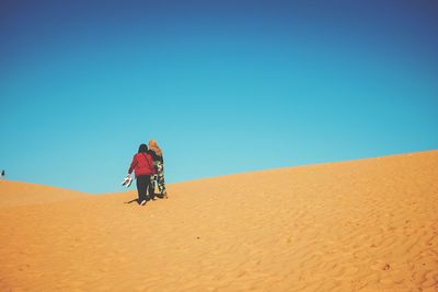 Person walking on sand dune in desert against clear sky