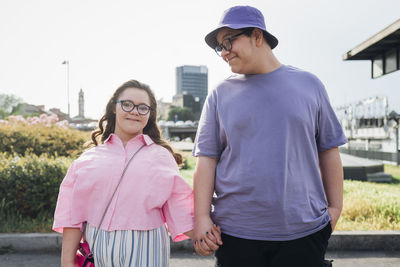 Teenage boy holding hand and looking at sister with down syndrome standing on footpath