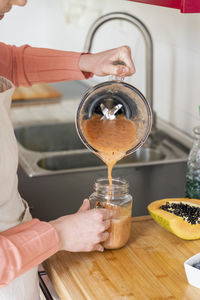 Young woman pouring smoothie in mason jar in kitchen at home