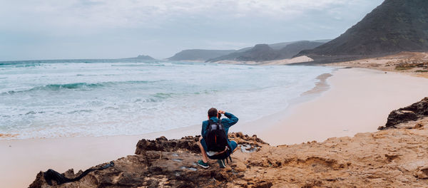 Rear view of man on rock at beach against sky