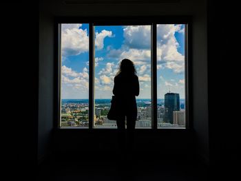 Rear view of woman looking at cityscape through window