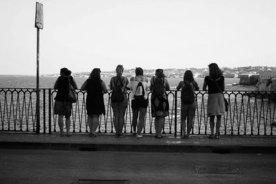 Rear view of people standing by railing against sea