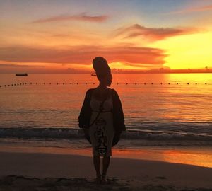 Woman standing on shore at beach against sky during sunset