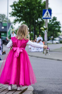 Full length of girl standing in pink dress putting flower on road