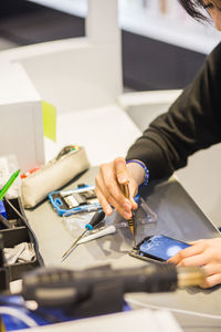 High angle view of young female employee repairing damaged smart phone at illuminated desk in mobile repair shop