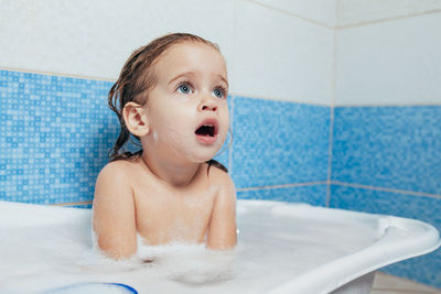 Cute girl looking away while sitting in bathtub