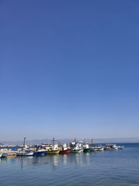 Sailboats moored in sea against clear blue sky