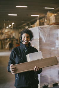 Smiling businesswoman with headset holding packages at warehouse