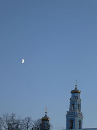 Low angle view of cross and buildings against clear blue sky