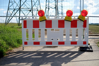 Red road sign by fence against sky