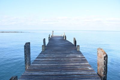 Wooden jetty leading to pier over sea against sky