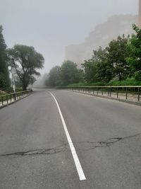 Empty road by trees against sky