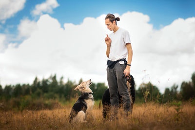 Man training dogs on grassy land against cloudy sky