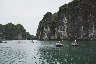 People rowing boat on halong bay by mountains