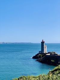 Lighthouse by sea against clear blue sky