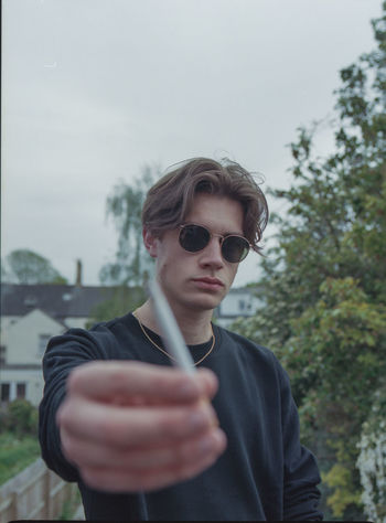 PORTRAIT OF YOUNG MAN WEARING SUNGLASSES STANDING AGAINST WALL