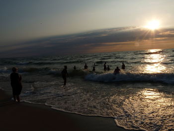 People on beach against sky during sunset