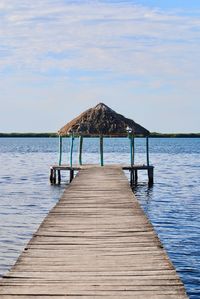 Wooden jetty leading to pier over sea against sky