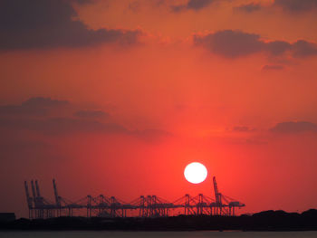 Silhouette cranes against orange sky during sunset