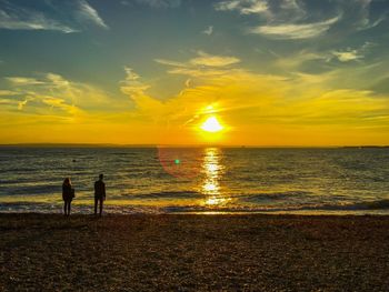 Silhouette people at beach against sky during sunset