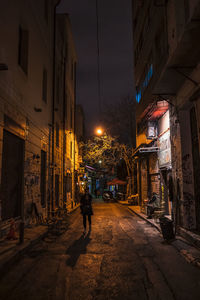 Man walking on illuminated street amidst buildings in city at night
