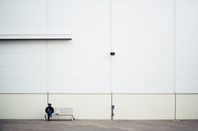 Man sitting on bench against white wall