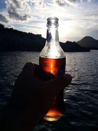 Close-up of hand holding wineglass against sky