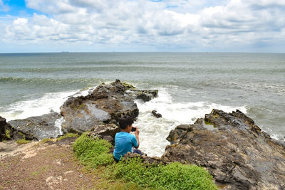 Boy on rock by sea against sky