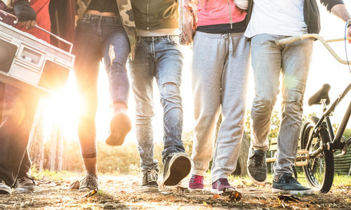 Low section of friends walking on field during sunset