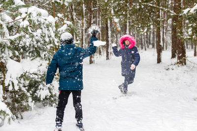 Boy swinging a snowball with a girl. funny children in winter park playing snowballs, actively