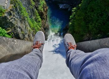 Low section of man sitting on cliff against river