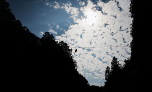 Distant view of silhouette person zip lining against sky