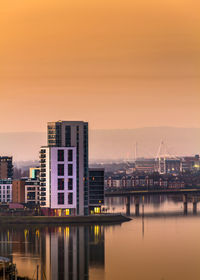 Illuminated city at waterfront during sunset