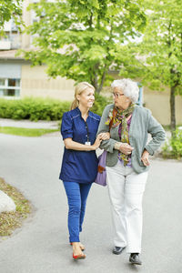 Full length of smiling female caretaker walking with senior woman on street