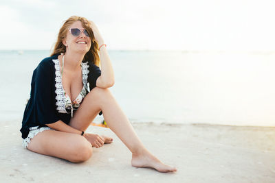 Happy female with sunglasses touching her hair sitting near the sea