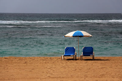 Chairs and parasol on beach against sky