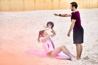 Fitness instructor assisting woman in exercising at beach