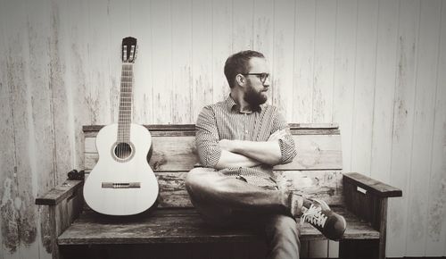 Man sitting by guitar on bench against wall