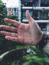 Cropped image of hand seen through wet glass window during rainy season