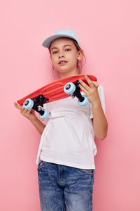 Portrait of young woman holding gun against pink background
