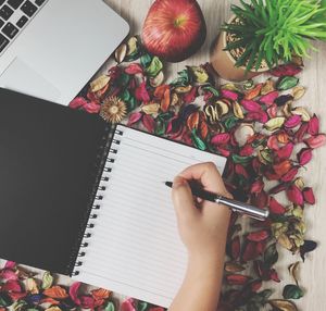 High angle view of person hand writing in diary by laptop on table