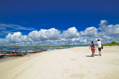 Rear view of people walking at beach against sky