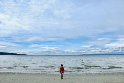 Rear view of little girl standing at beach against sky. tiny human, big world.