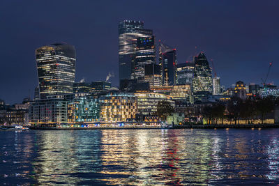Illuminated buildings by river against sky at night