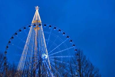 Low angle view of ferris wheel and christmas tree against clear night sky