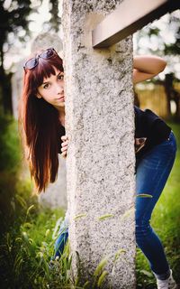 Portrait of young woman standing against tree trunk