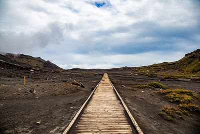 Dirt road leading towards mountain against sky